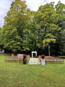 The ceremony is set in the yard with majestic maples in the background and rose petals in the aisle