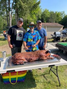 Friends smile behind a perfectly roasted pig from Shaws DIY Pig Roast